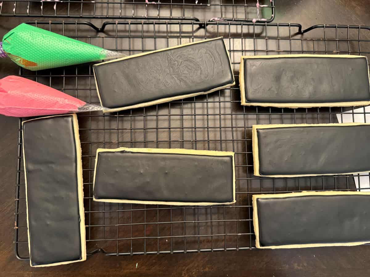 black royal icing cookies with piping bags with green and pink royal icing in piping bags