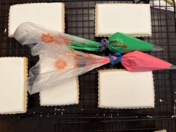 white royal icing cookies with piping bags filled with green and pink royal icing