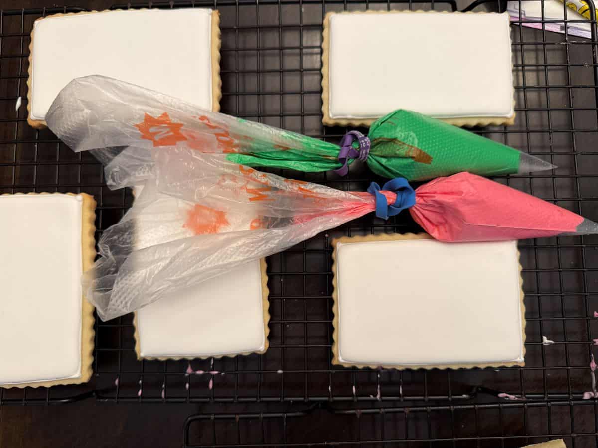 white royal icing cookies with piping bags filled with green and pink royal icing