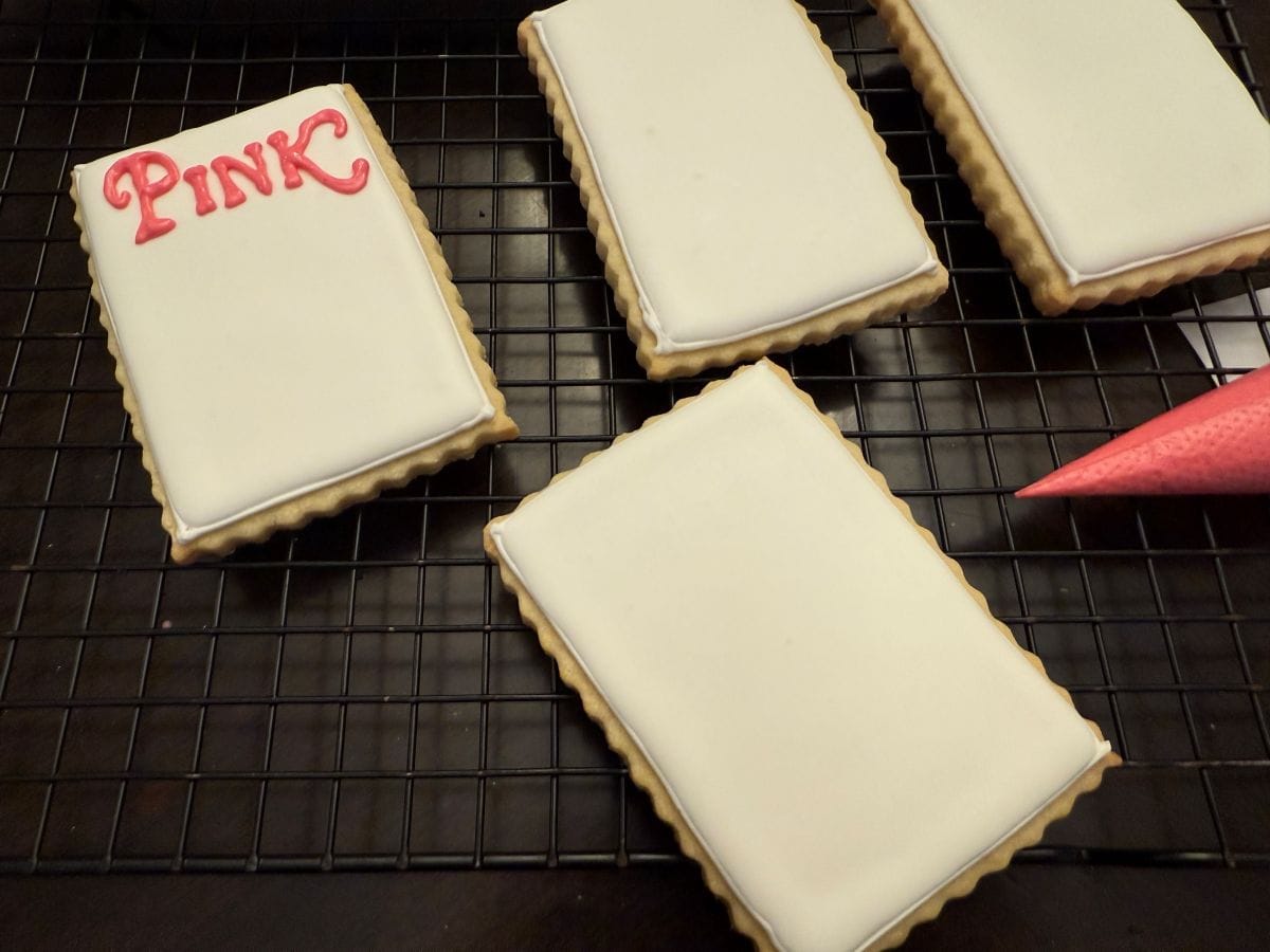 white royal icing cookies with the word "pink" piped in pink royal icing