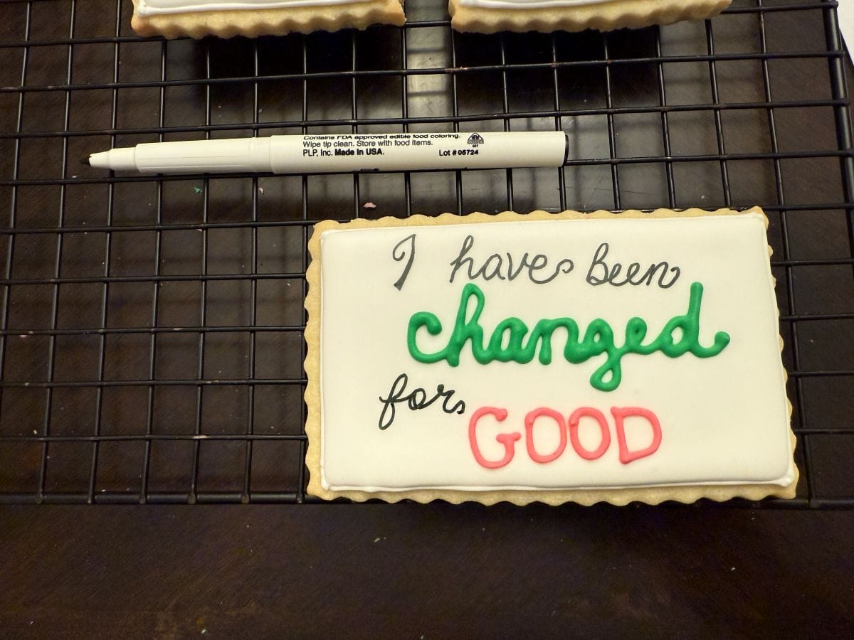 a white royal icing cookie next to a black edible marker that says "I have been changed for good"