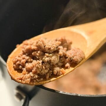 Homemade Italian Turkey Sausage on a wooden spoon held over a stock pot