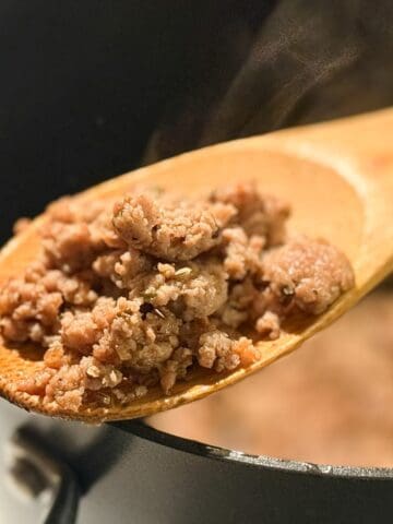 Homemade Italian Turkey Sausage on a wooden spoon held over a stock pot