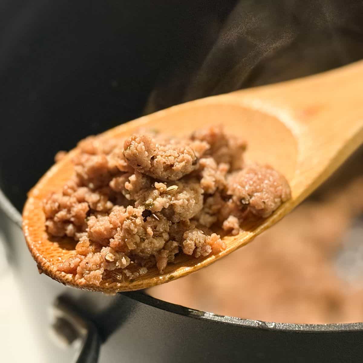 Homemade Italian Turkey Sausage on a wooden spoon held over a stock pot