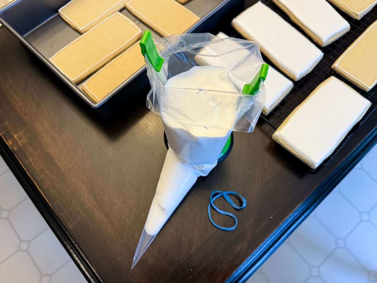 diluted flood consistency white royal icing in a piping bag held up by a piping bag holder