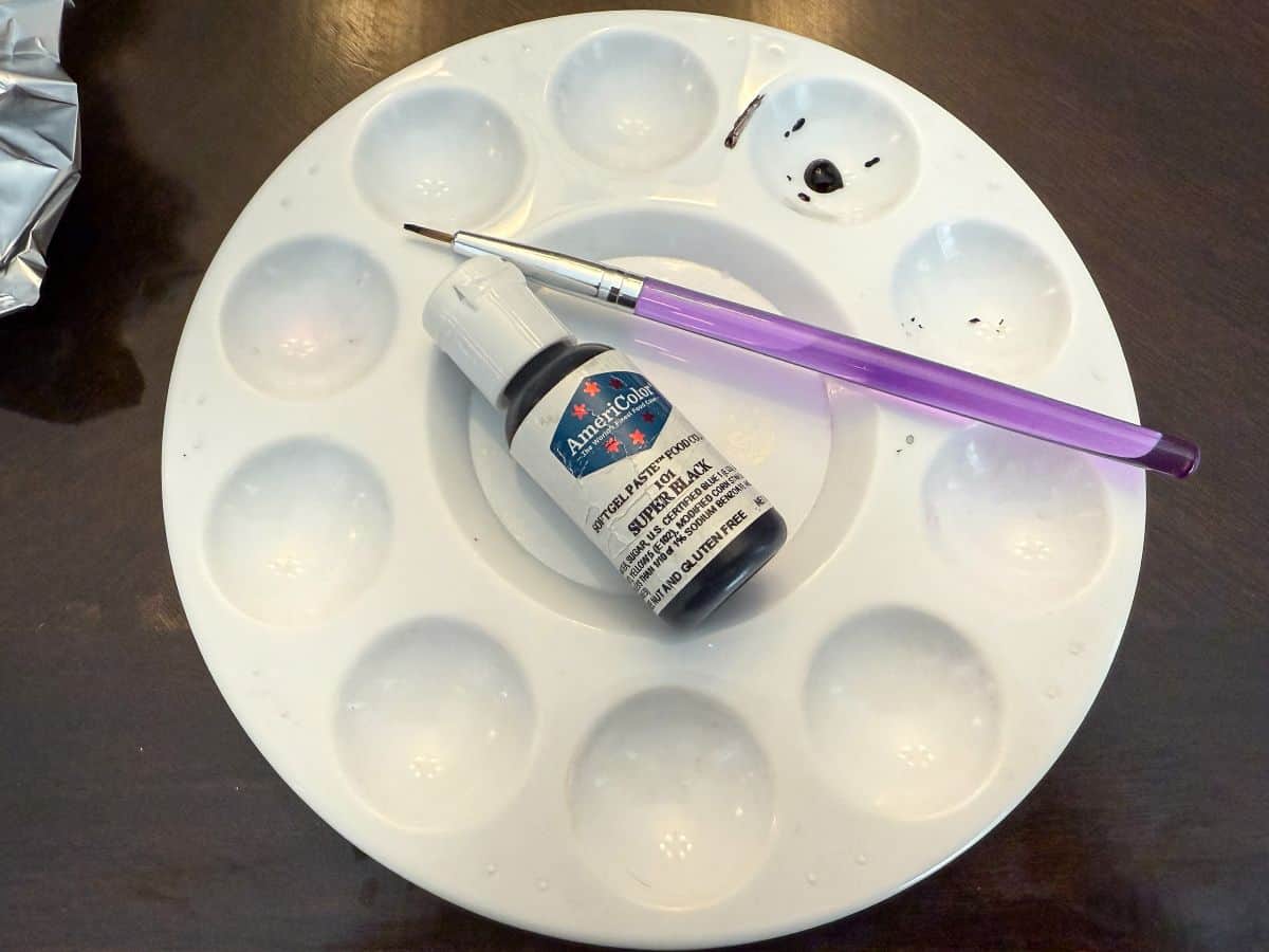 black food coloring gel bottle in the center of a paint palette with a food grade paintbrush