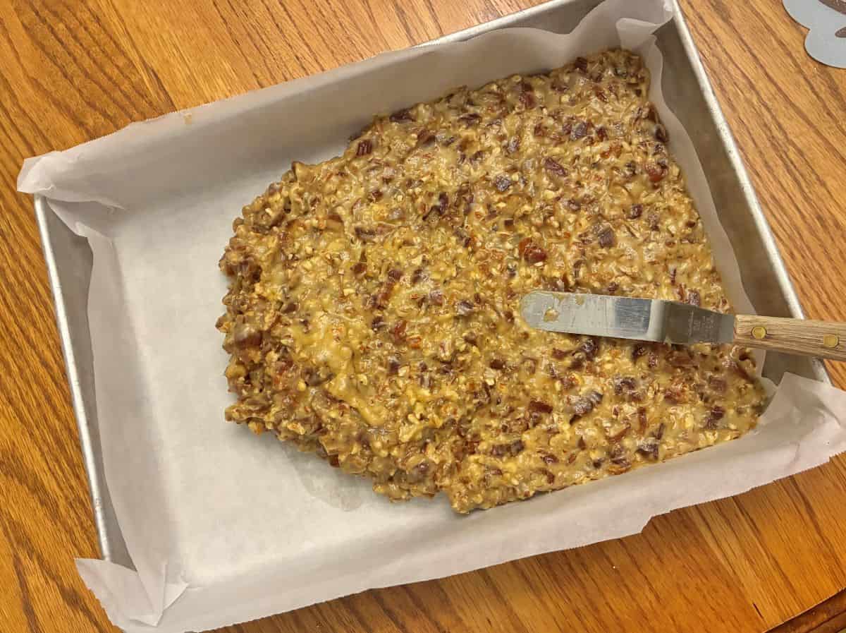 Date Bar batter being spread into a parchment paper lined rectangular cake pan