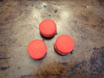 three assembled red macarons on a baking sheet