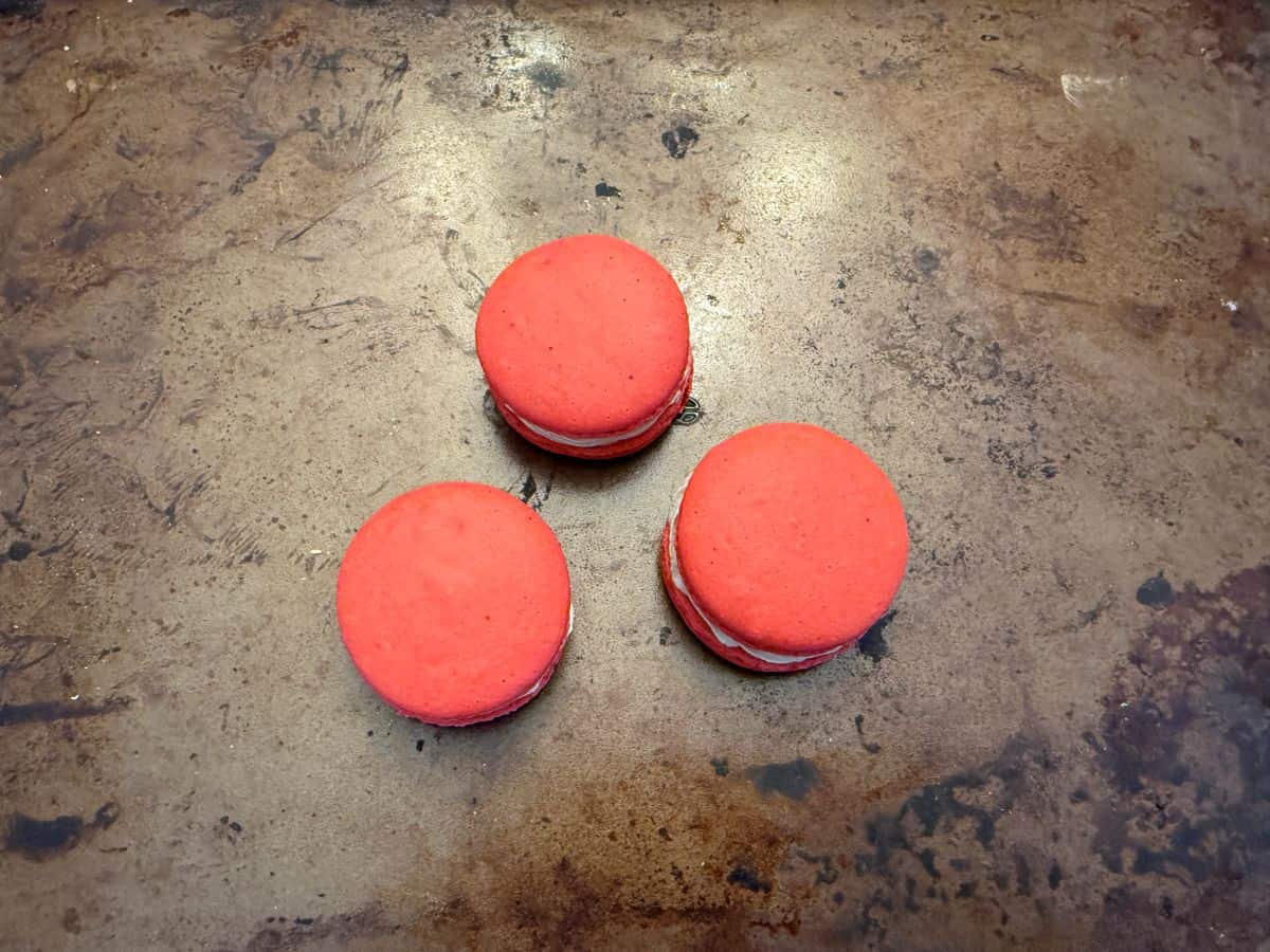 three assembled red macarons on a baking sheet