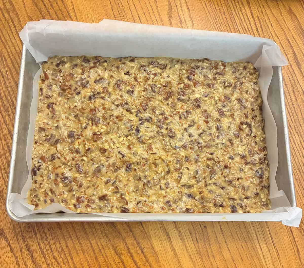 Date Bar batter spread evenly in a parchment paper lined rectangular cake pan