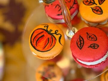 an orange macaron with a darker orange pumpkin outlined in black painted on top