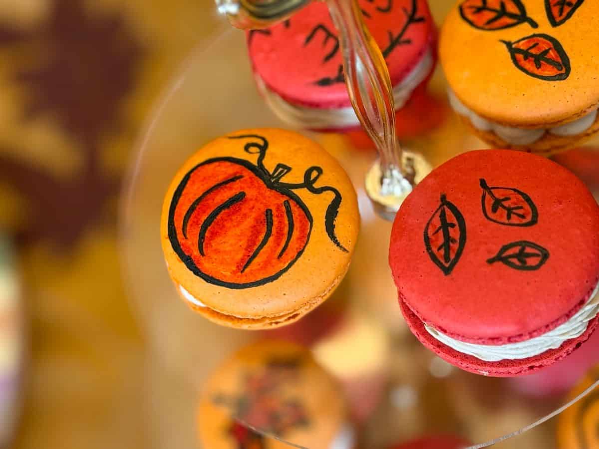 an orange macaron with a darker orange pumpkin outlined in black painted on top