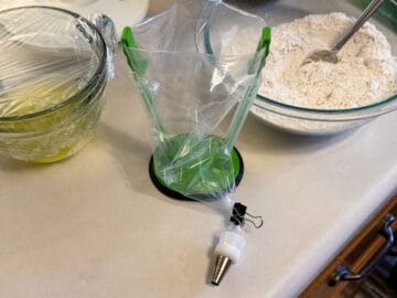 an empty disposable piping bag in a piping bag holder with a metal tip attached and secured with a small binder clip