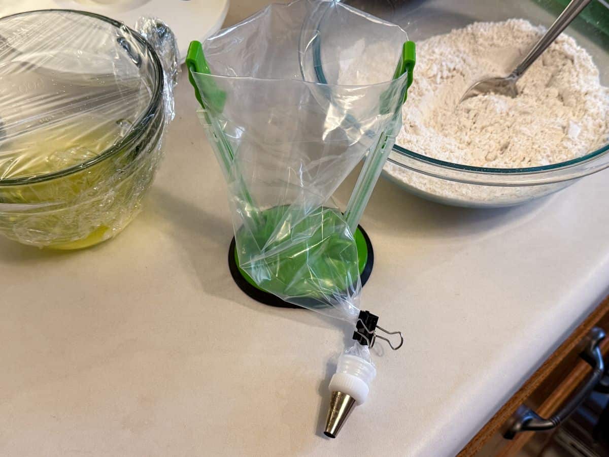 an empty disposable piping bag in a piping bag holder with a metal tip attached and secured with a small binder clip