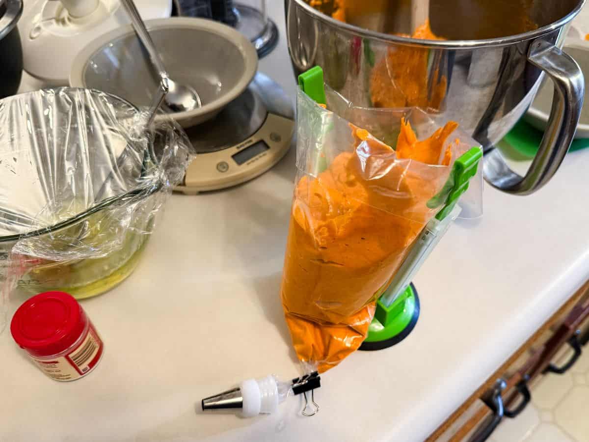 orange macaron batter filling a disposable piping bag being held open by a piping bag holder