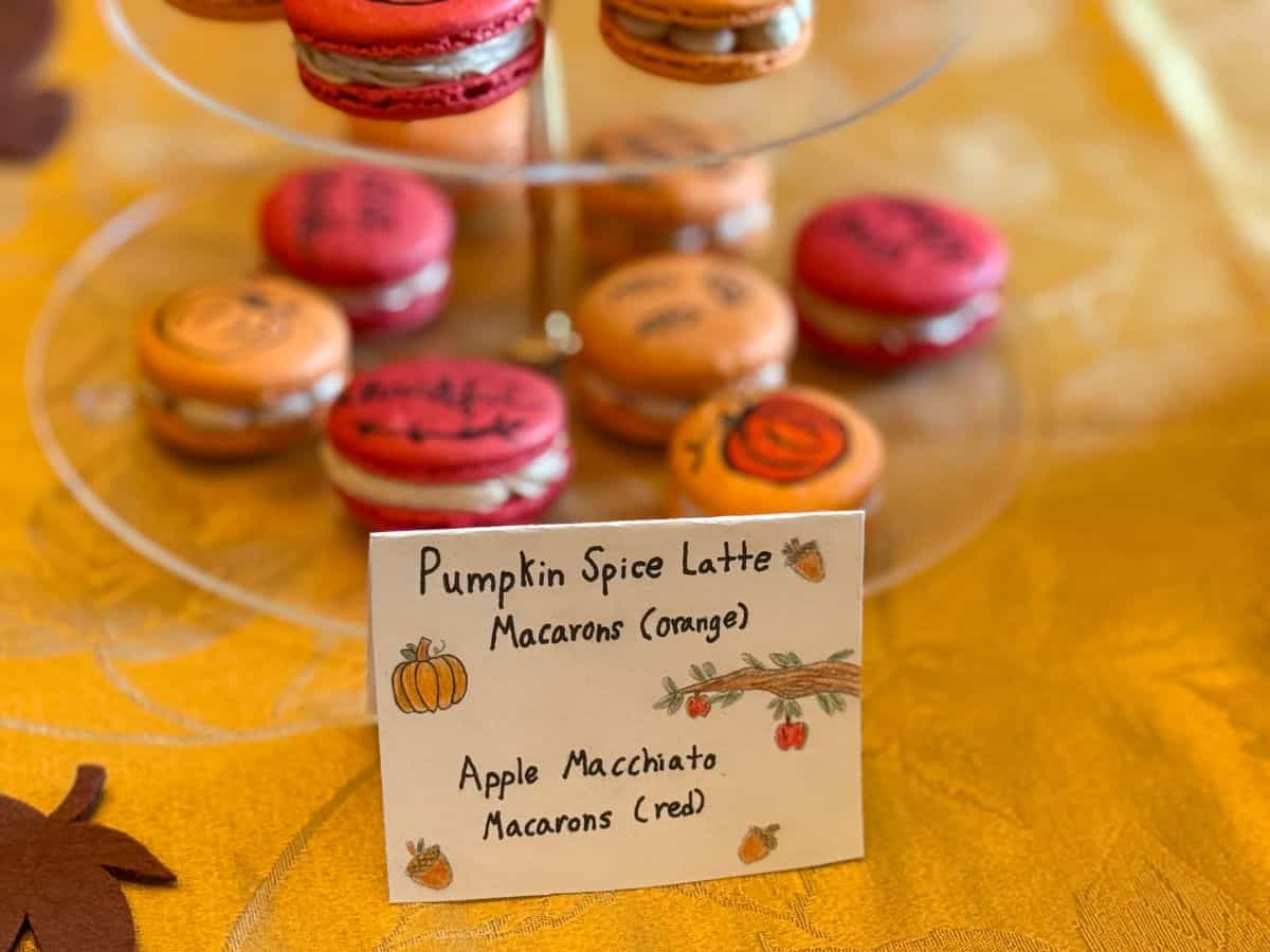 a sign that says Pumpkin Spice Latte Macarons and Apple Macchiato Macarons in front of a 3-tiered server of fall decorated macarons