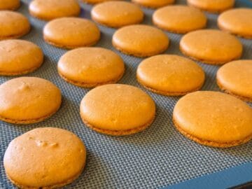 orange macaron shells cooling on a macaron mat