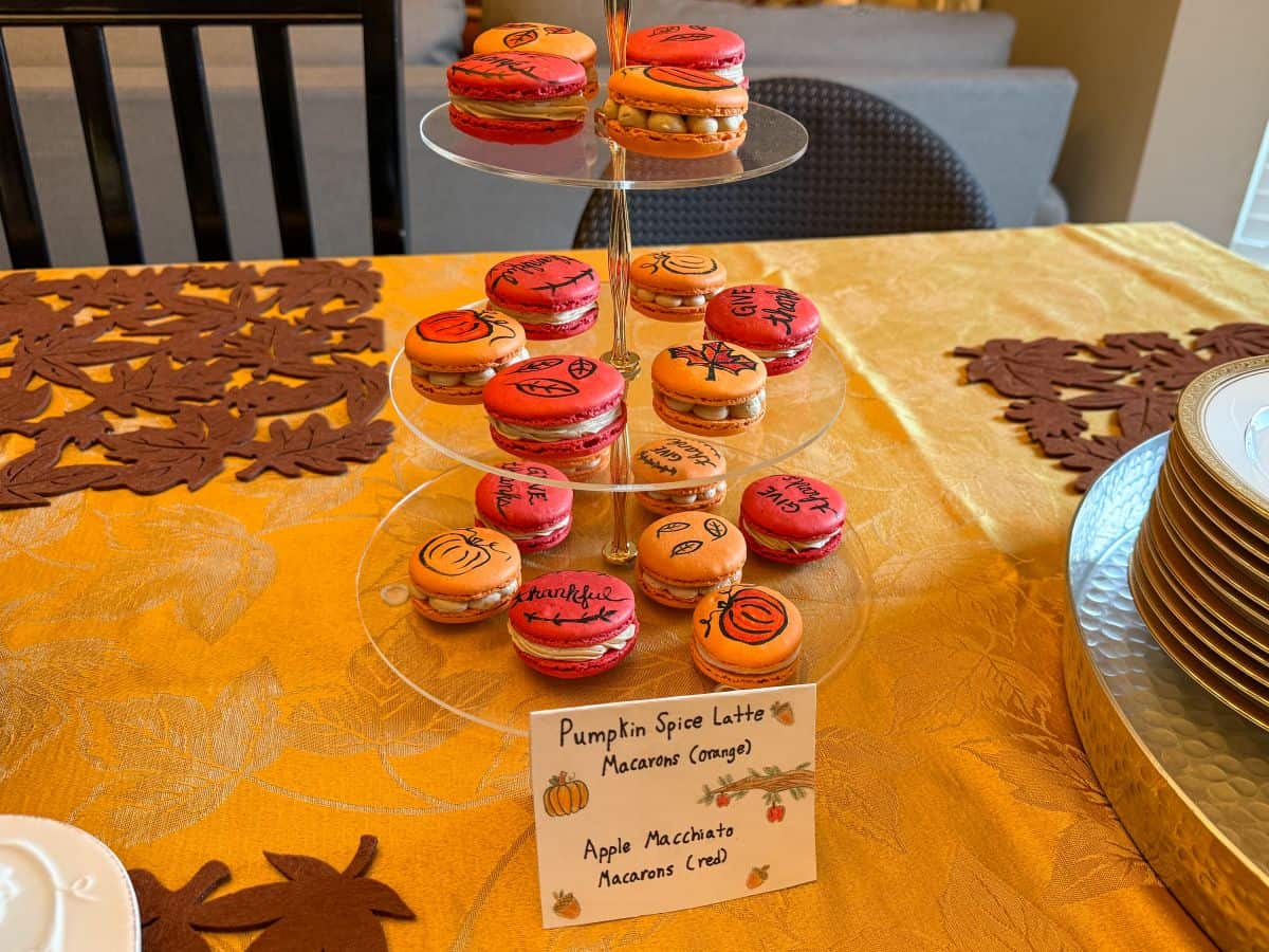 a sign that says Pumpkin Spice Latte Macarons and Apple Macchiato Macarons in front of a 3-tiered server of fall decorated macarons