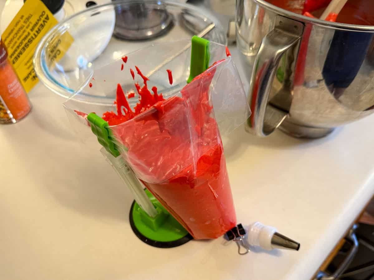 red macaron batter in a clear disposable piping bag held open with a piping bag holder