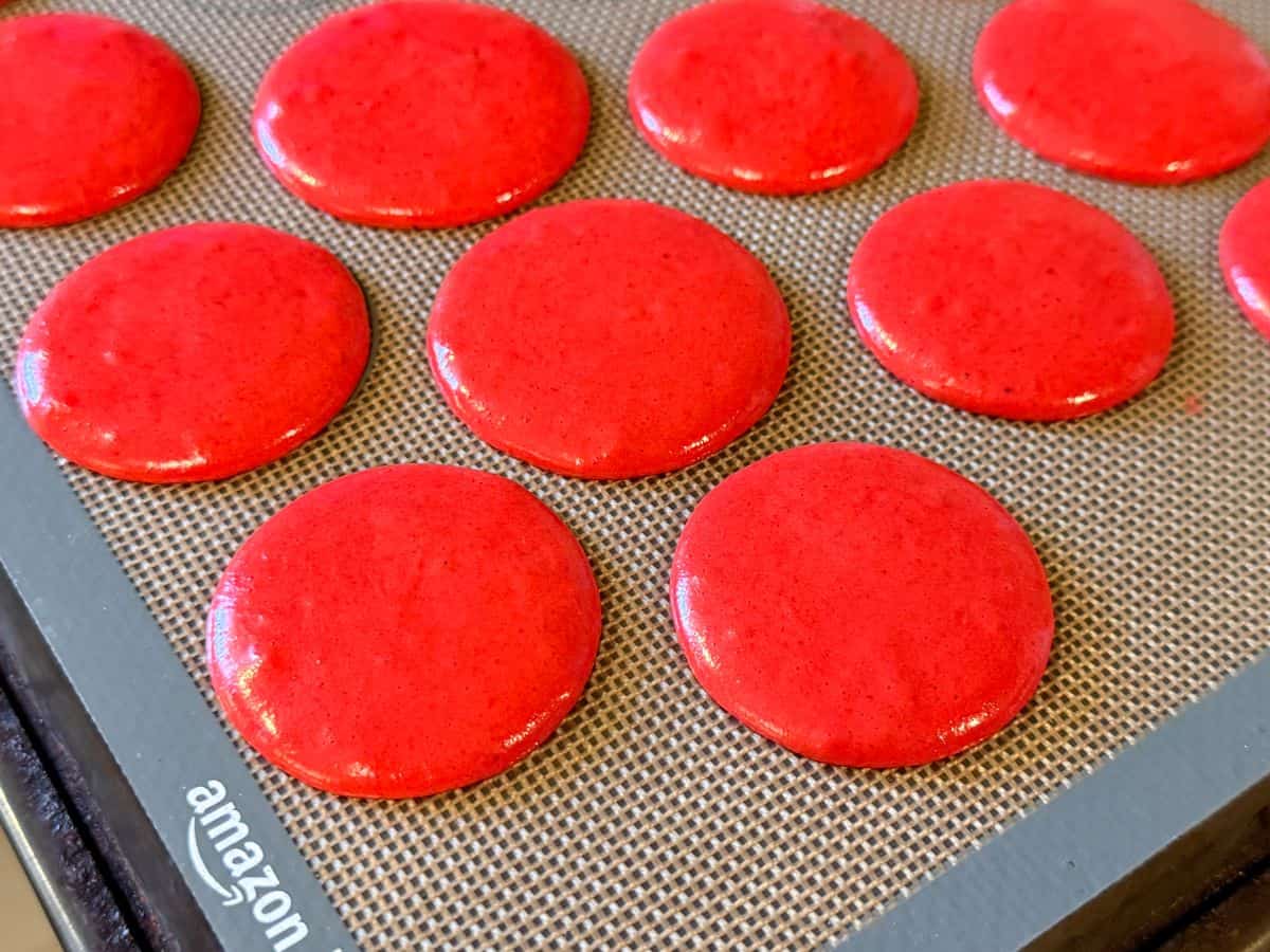 macaron batter piped into circles on a macaron mat during the rest step