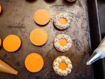 three orange macaron shells with piped dots of coffee buttercream as borders