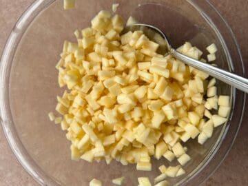 small pieces of apple chopped in a glass bowl with a metal spoon in the bowl