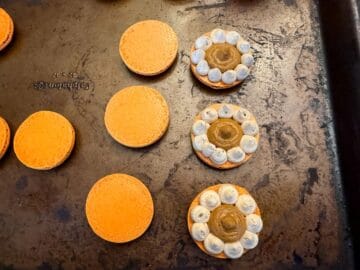 three macaron shells with coffee buttercream borders filled with pumpkin filling next to three top shells
