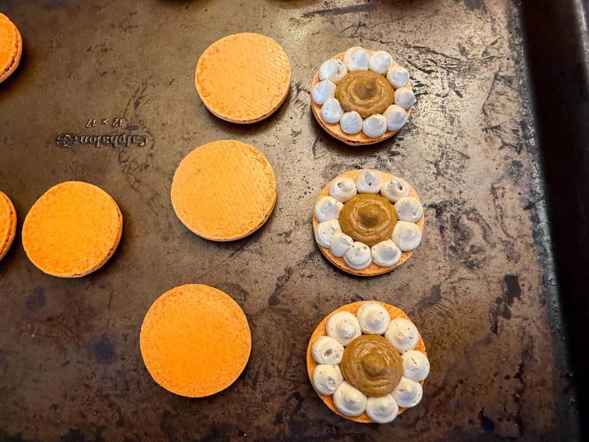 three macaron shells with coffee buttercream borders filled with pumpkin filling next to three top shells