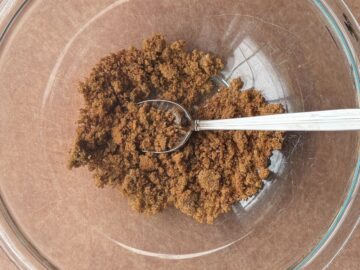 a mixture of brown sugar and spices in a glass bowl with a metal spoon