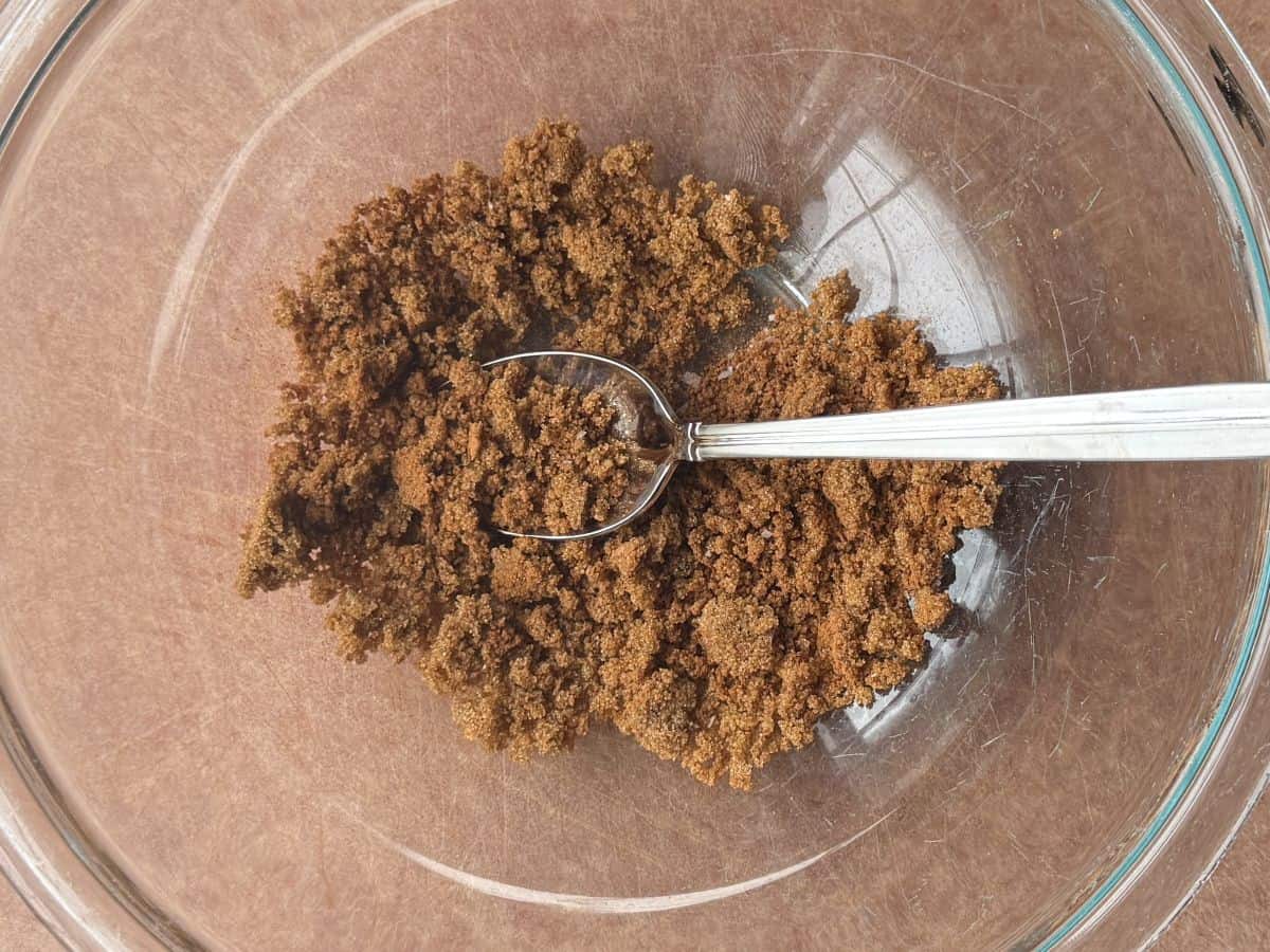 a mixture of brown sugar and spices in a glass bowl with a metal spoon