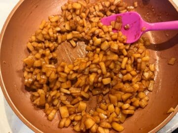 caramel apple filling being cooked in a saucepan on the stove and stirred with a small pink silicone spatula