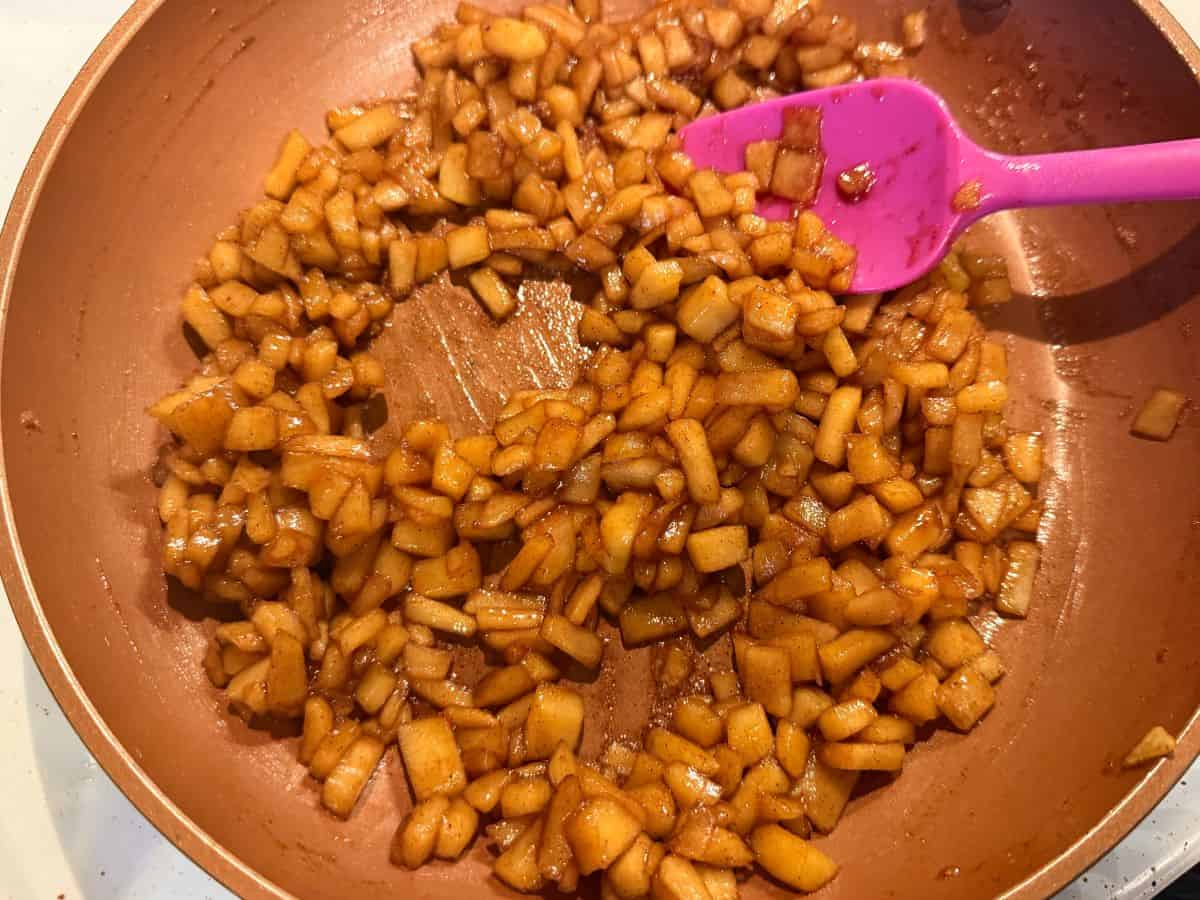 caramel apple filling being cooked in a saucepan on the stove and stirred with a small pink silicone spatula