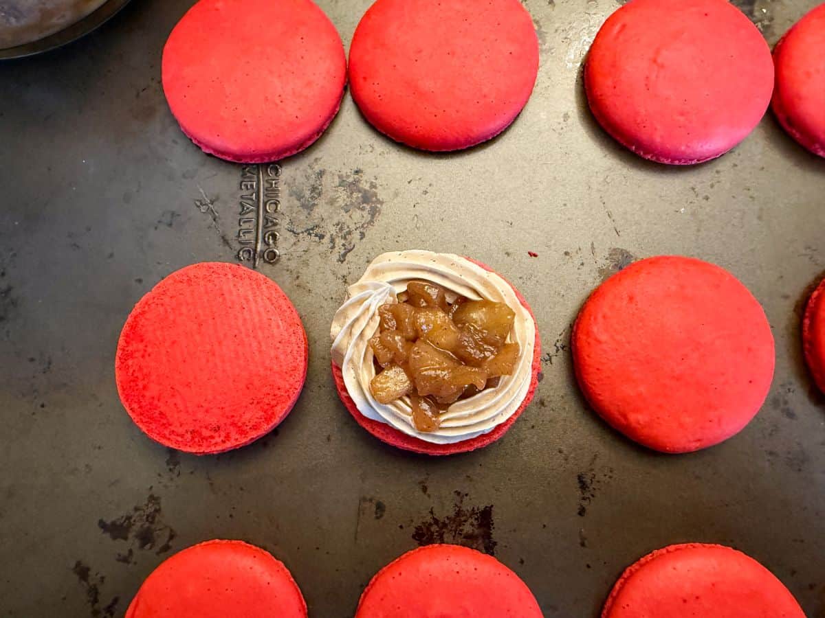 coffee buttercream piped around the border of a red macaron shells with caramel apple filling inside