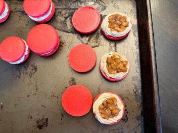 coffee buttercream piped around the border of 3 red macaron shells with caramel apple filling inside