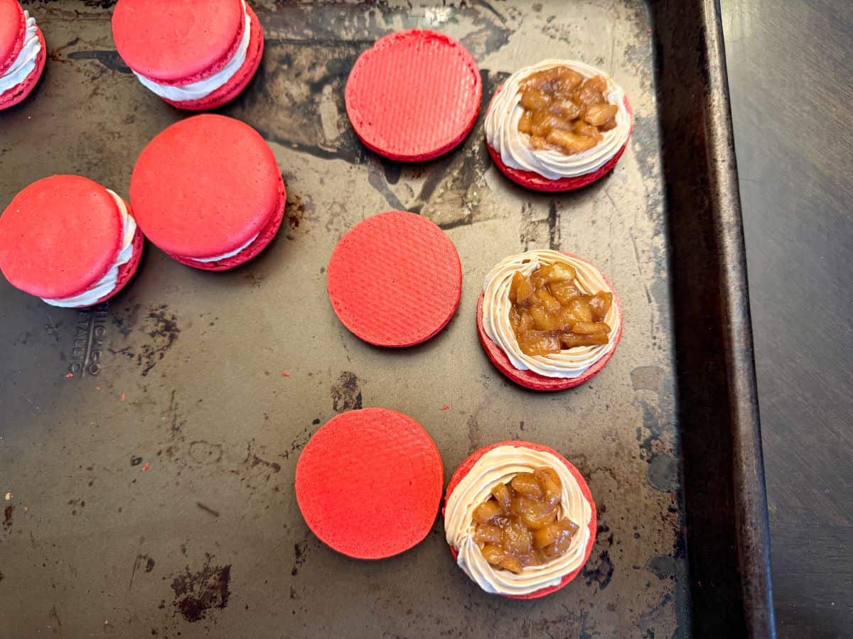 coffee buttercream piped around the border of 3 red macaron shells with caramel apple filling inside