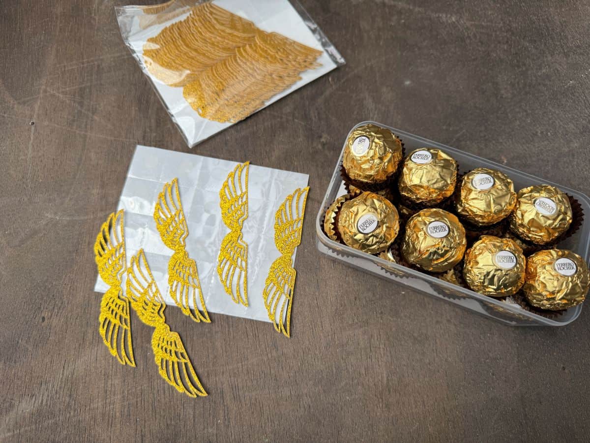 flat gold glitter cardstock wings next to a tray of Ferrero Rocher candies