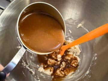 butterscotch sauce being poured from a measuring cup into a stand mixer bowl containing buttercream