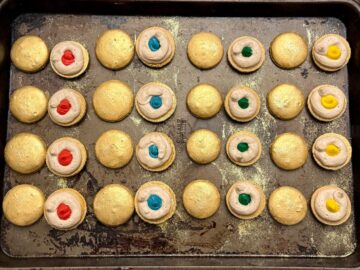 gold macarons paired up with butterscotch buttercream dam around some and filled with colored buttercream