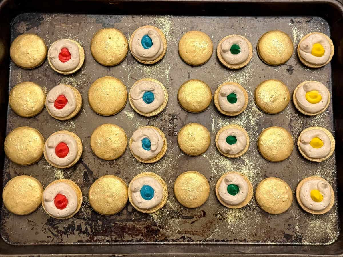 gold macarons paired up with butterscotch buttercream dam around some and filled with colored buttercream