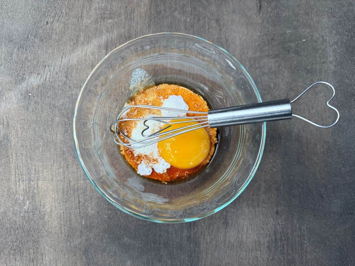 egg, vanilla and cream in a small glass bowl with a small wire whisk
