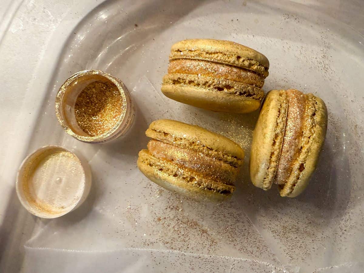 edible gold glitter being added to the side filling of gold macarons