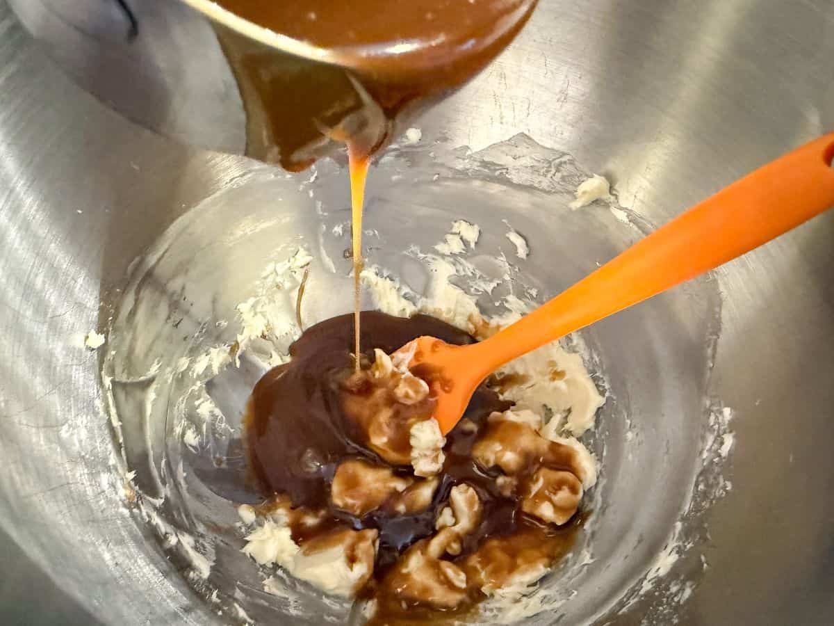 butterscotch sauce being poured from a measuring cup into a stand mixer bowl containing buttercream
