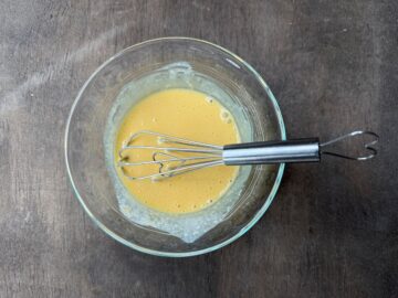 mixed up egg, cream and vanilla in a glass bowl with a wire whisk