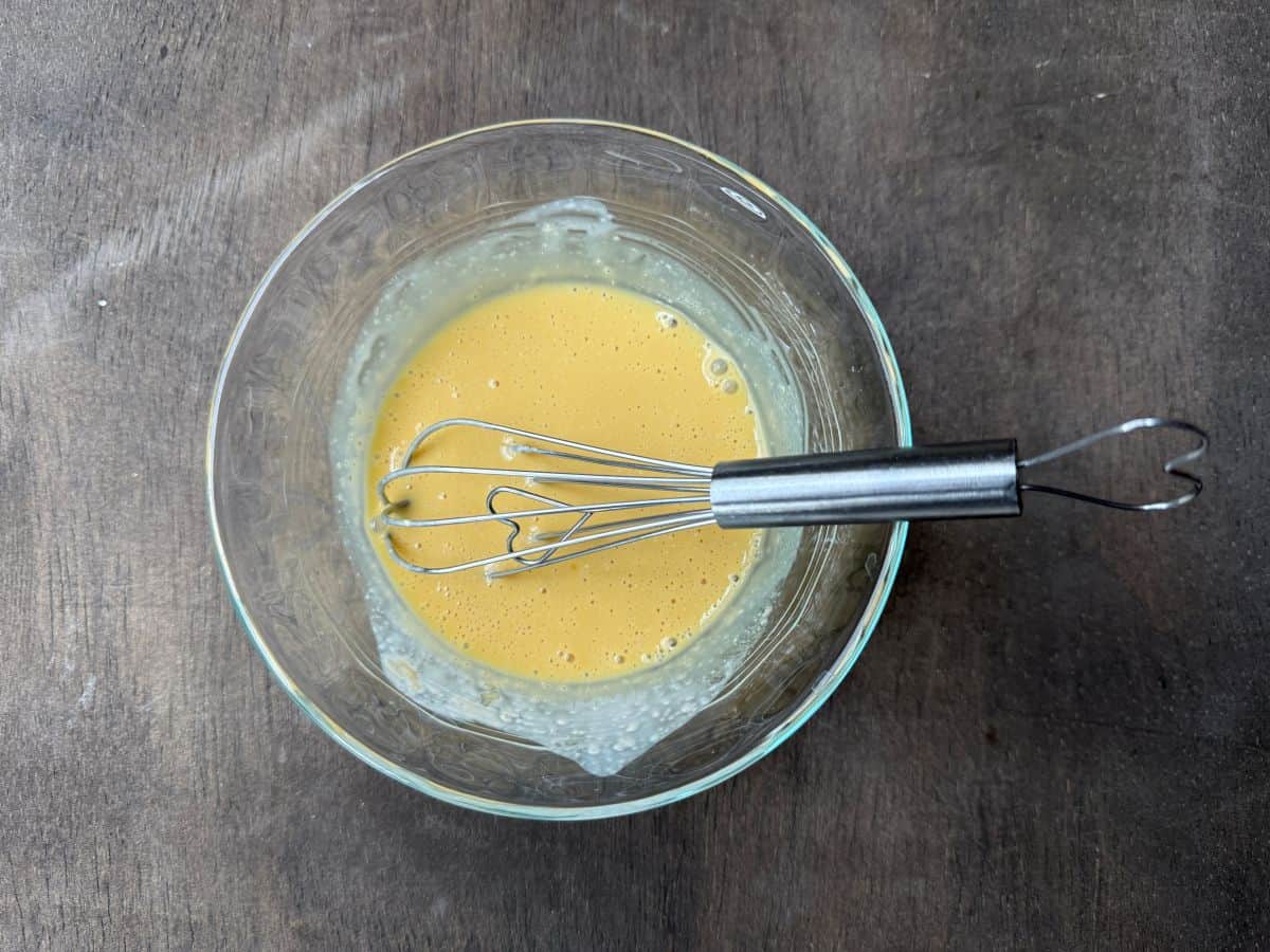 mixed up egg, cream and vanilla in a glass bowl with a wire whisk