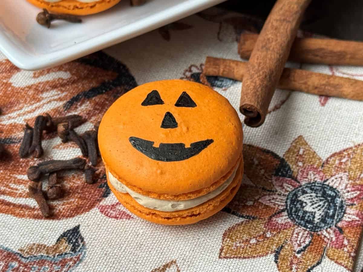 a Nut Free Halloween Macaron on a fall themed towel next to cinnamon sticks and whole coffee beans