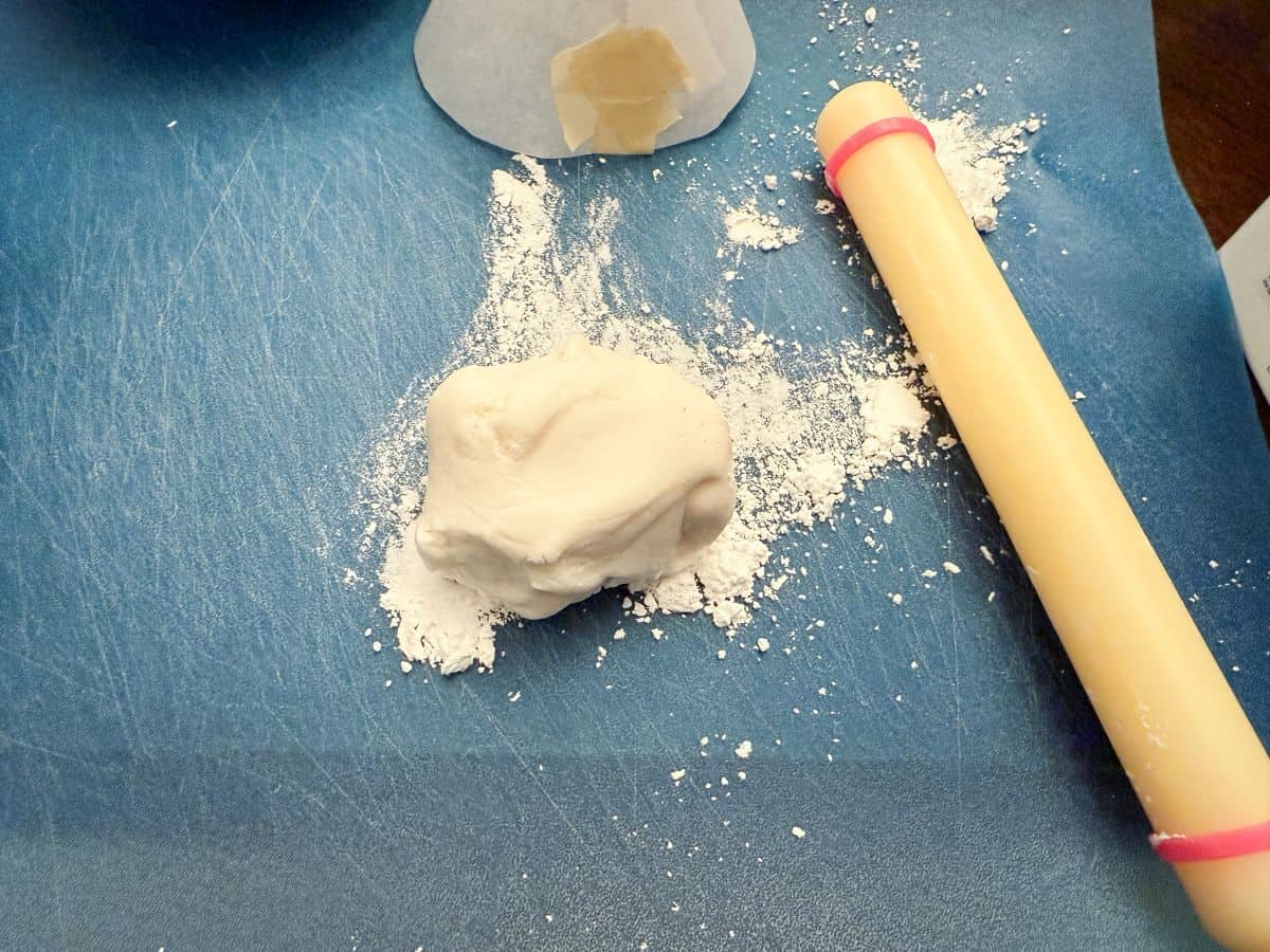 white fondant on a cutting mat with powdered sugar underneath next to a small fondant rolling pin