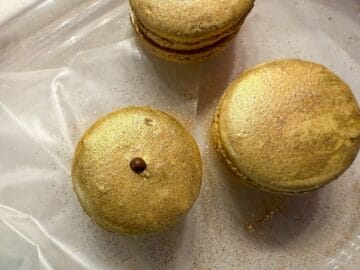 a gold macaron with a dot of melted chocolate on top