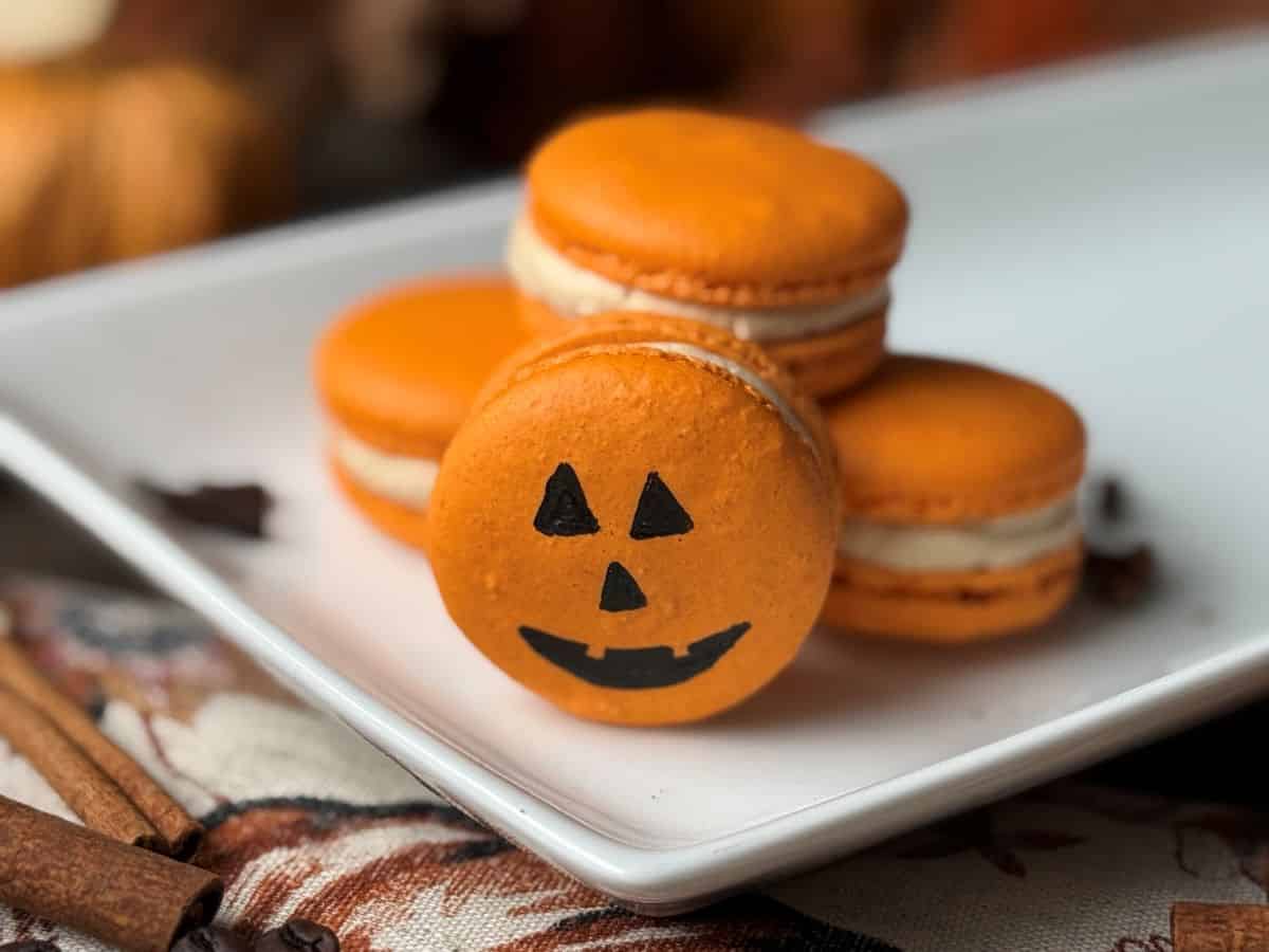Orange Halloween pumpkin macarons with black jack-o'-lantern face design.