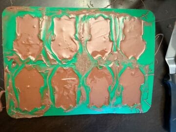 a green silicone frog mold filled with melted chocolate
