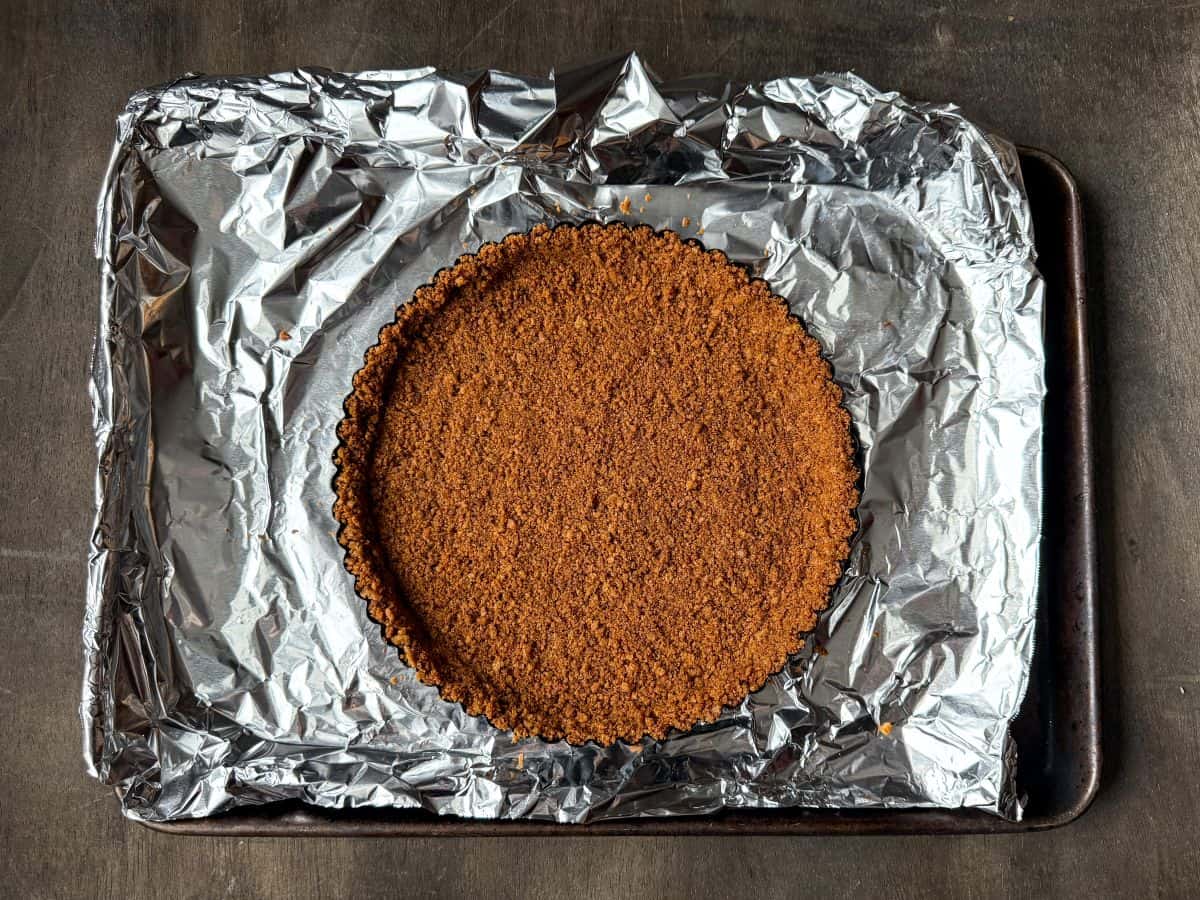 a gingersnap cookie crust pressed into a tart pan on a foil lined baking sheet before baking